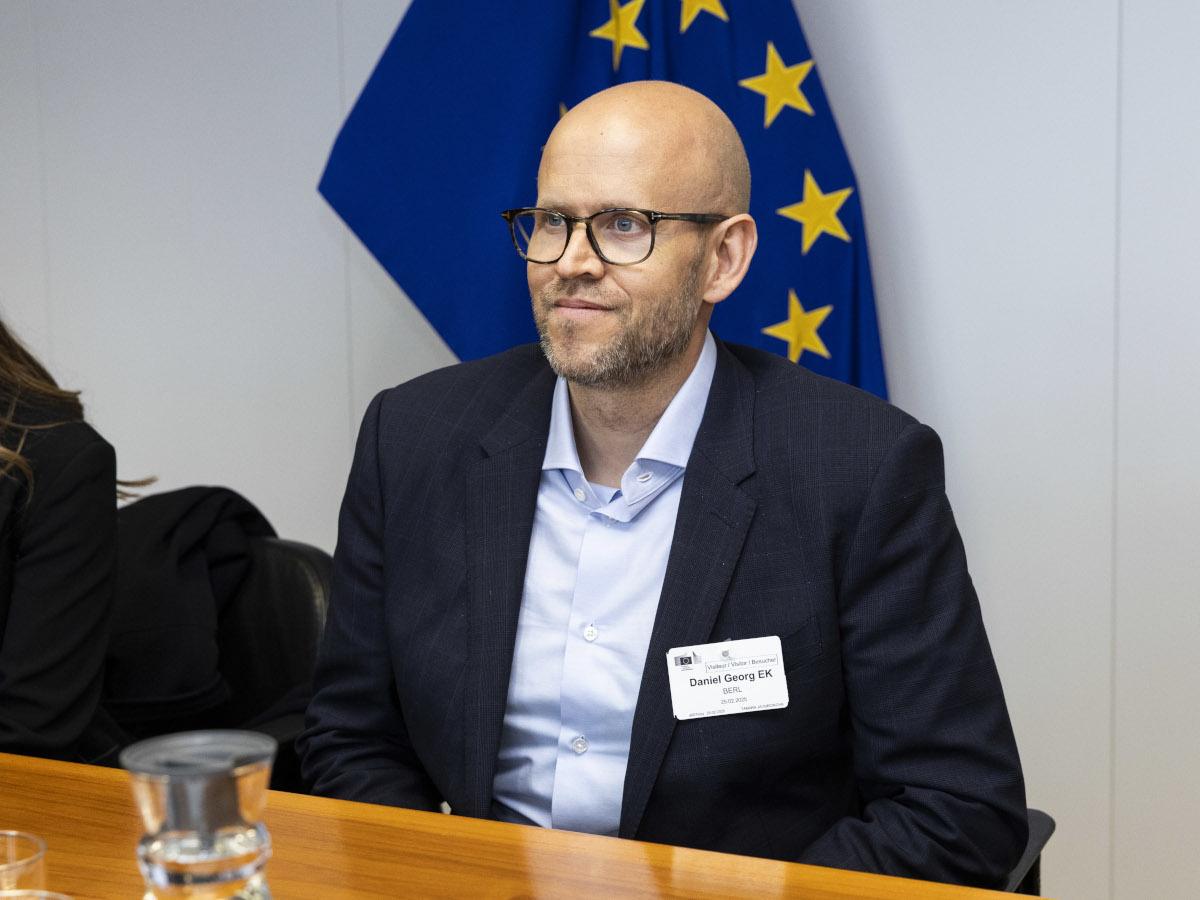 Daniel Ek wears a dark suit, pale blue shirt and dark glasses and sits in an EU board room.